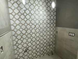 Modern bathroom renovation in progress showing geometric wall tiles and grey floor tiles, with exposed plumbing.