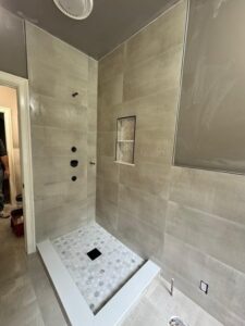 Bathroom Tile Installation in Progress – Detailed view of the shower area with beige wall tiles, a framed niche, and white shower base.