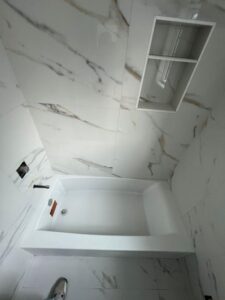 Modern bathtub installation with marble imitation tiles in a bathroom renovation.