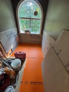 Bathroom Tile Installation in Progress – A view of the bathroom under construction with an orange tile underlayment for floor installation and wall tiles in progress.
