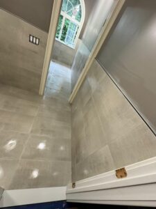 Bathroom Tile Installation in Progress – A corner view of the bathroom with beige tiles installed on the walls and floor, and a window in the background.