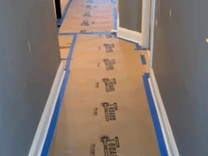 Hallway painting project with protective boards covering the floor and taped baseboards.