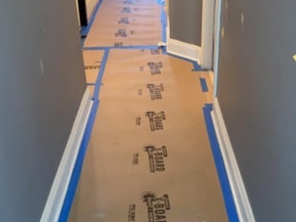 Hallway painting project with protective boards covering the floor and taped baseboards.