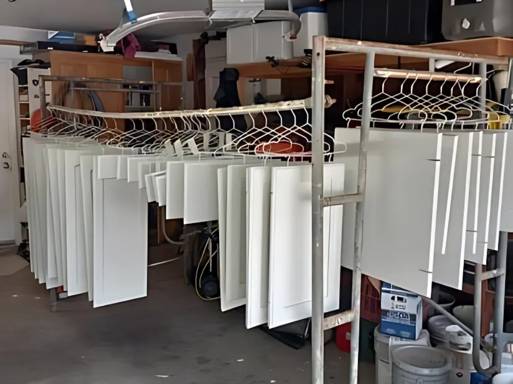 Cabinet doors and drawers hanging in a garage, drying after refinishing and painting.