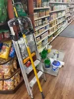 supermarket wall painting preparation with ladder and paint materials in aisle.