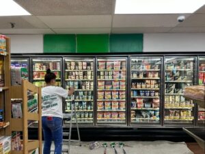 worker applying supermarket wall painting above refrigerated display units.