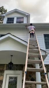 Deck refinishing and exterior painting with technician working on upper soffit area.