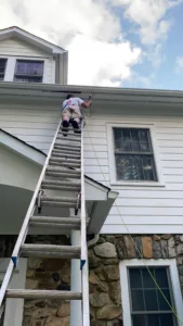 Deck refinishing and exterior painting showing exterior soffit work on ladder.