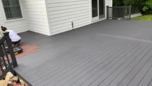 Deck refinishing and exterior painting with worker applying coating on deck boards.